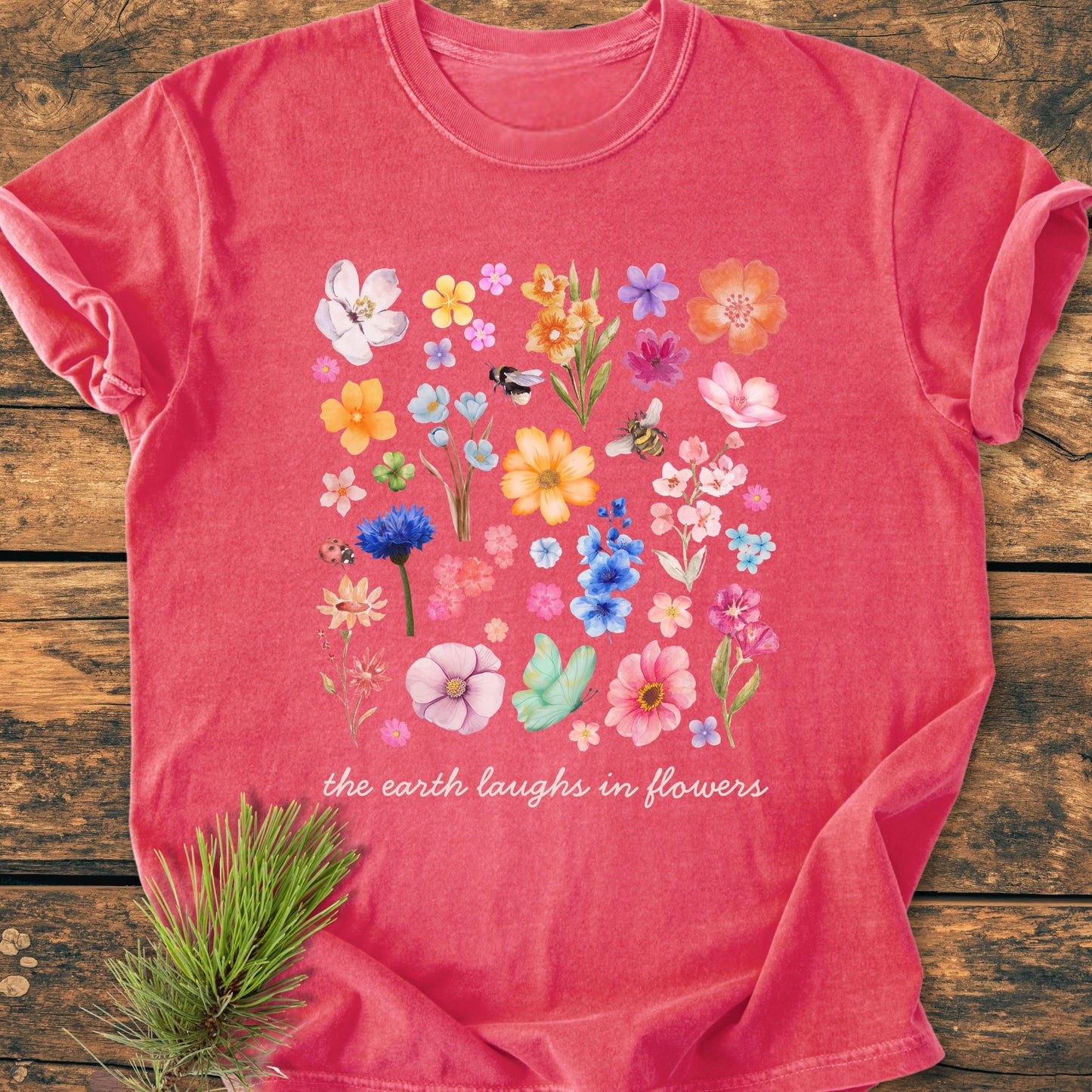 The Earth Laughs In Flowers - Vintage Heavyweight Tee features a grid of watercolor-style flowers with insects and the phrase on a heathered red T-shirt, styled with a pine sprig.