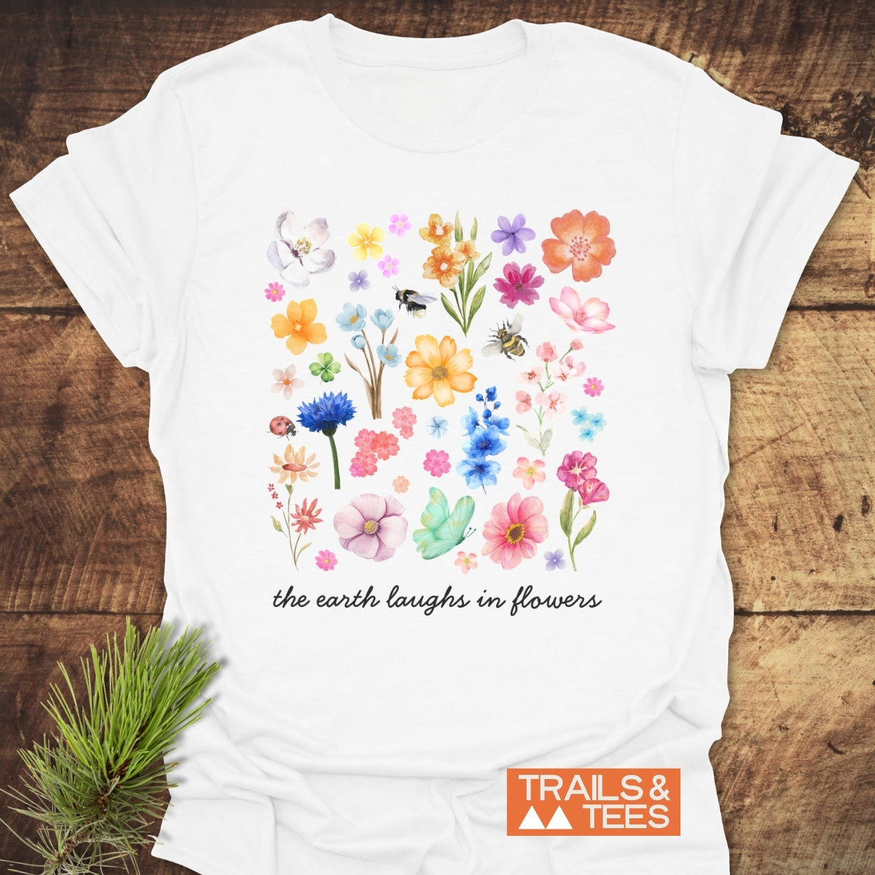 The Earth Laughs In Flowers T-Shirt features colorful flower illustrations and insects on white cotton, embodying outdoor adventure and comfort from Trails & Tees.