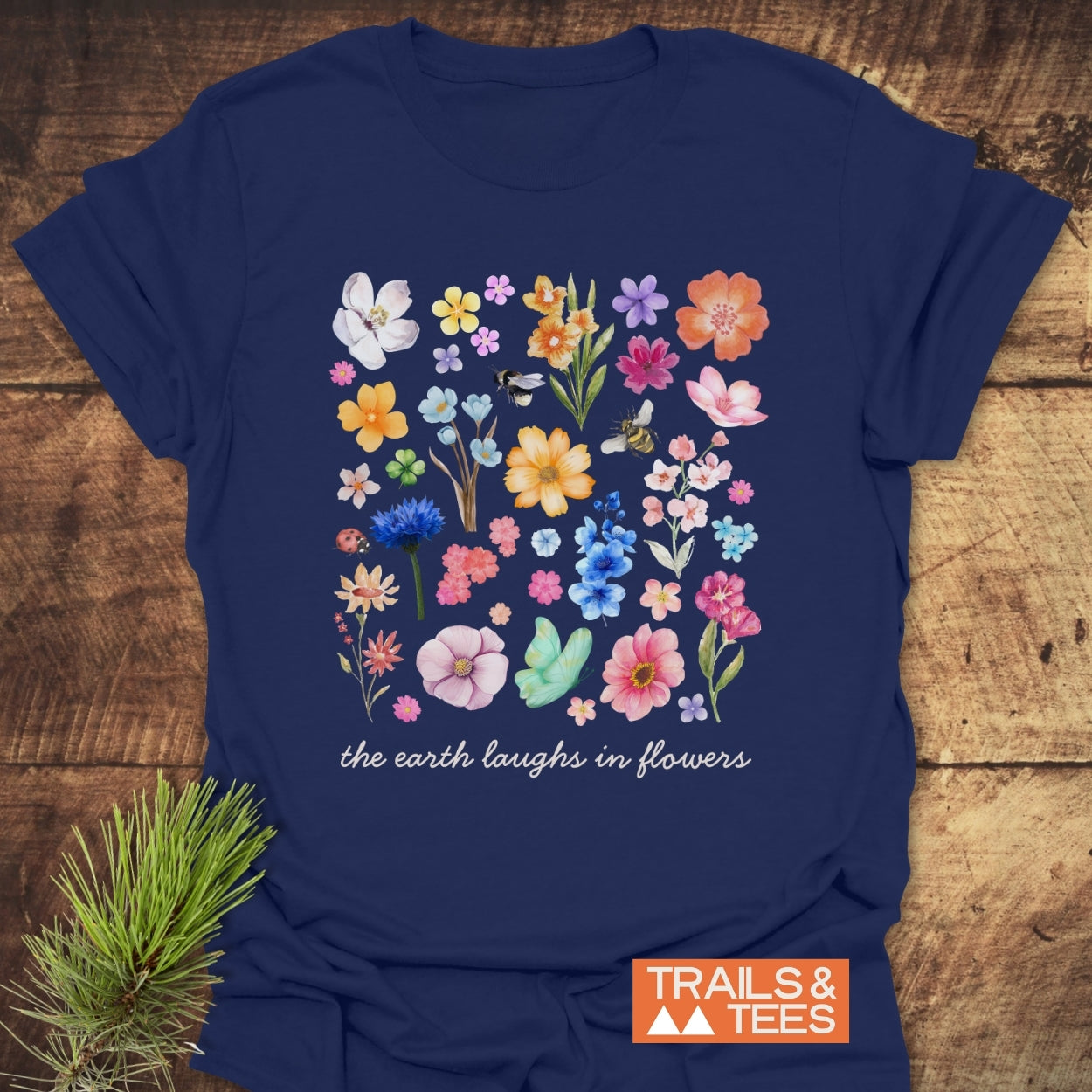 The Earth Laughs In Flowers T-Shirt displays a vibrant floral grid with insects and the slogan, crafted from soft cotton, ideal for outdoor adventures. Features durable prints and sustainable, on-demand production.