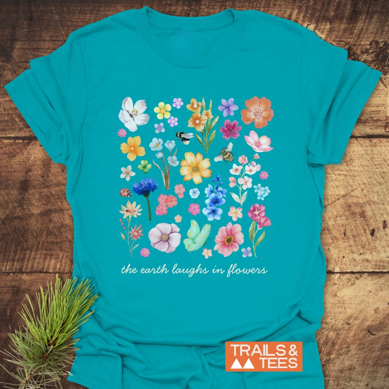 The Earth Laughs In Flowers T-Shirt features watercolor wildflowers with bees and a ladybug on soft cotton, conveying a love for nature and adventure.