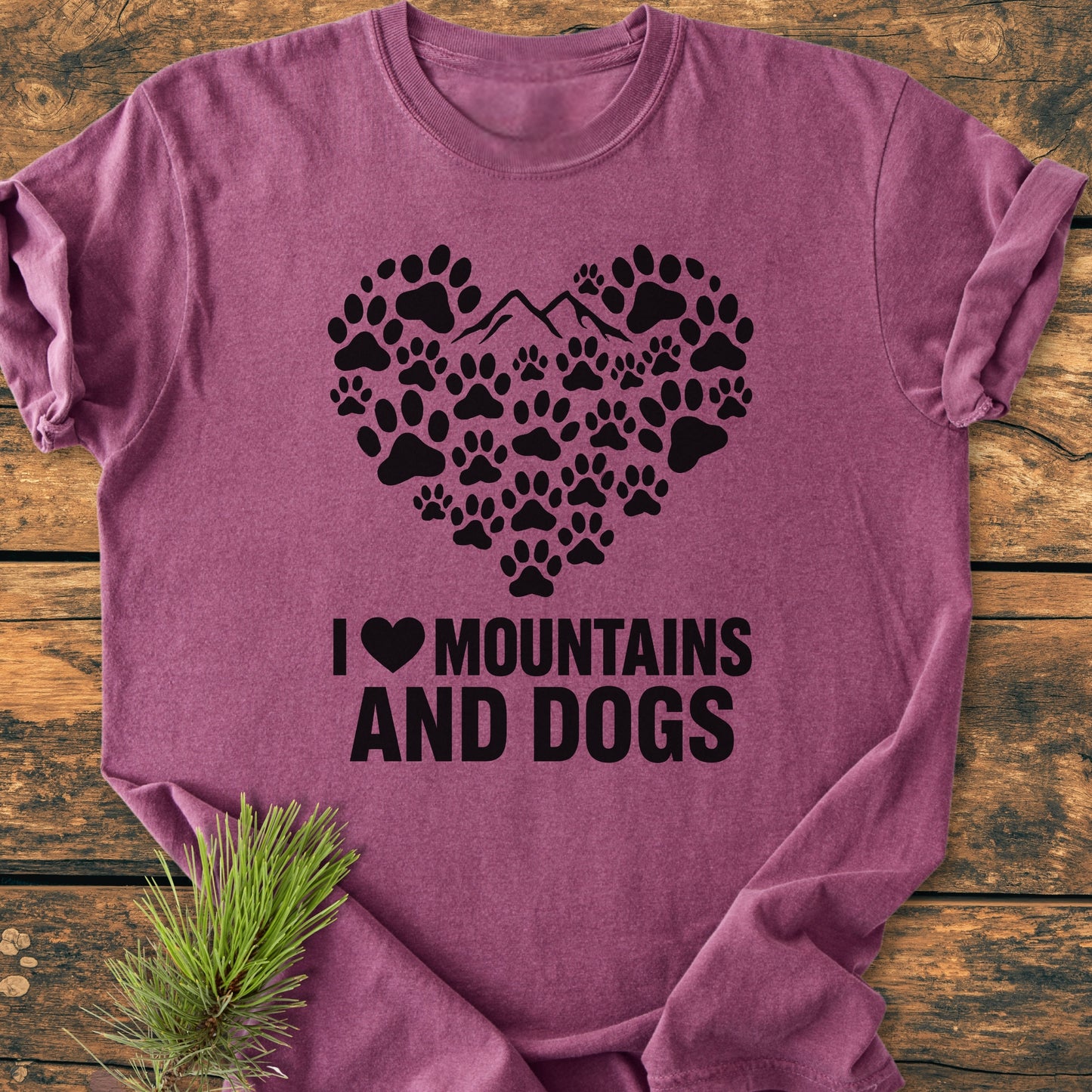 Paw Heart Dog Lover - Vintage Heavyweight Tee features a heart graphic of dog paw-prints and mountains with “I ♥ MOUNTAINS AND DOGS” text, styled with a pine sprig on wooden surface.