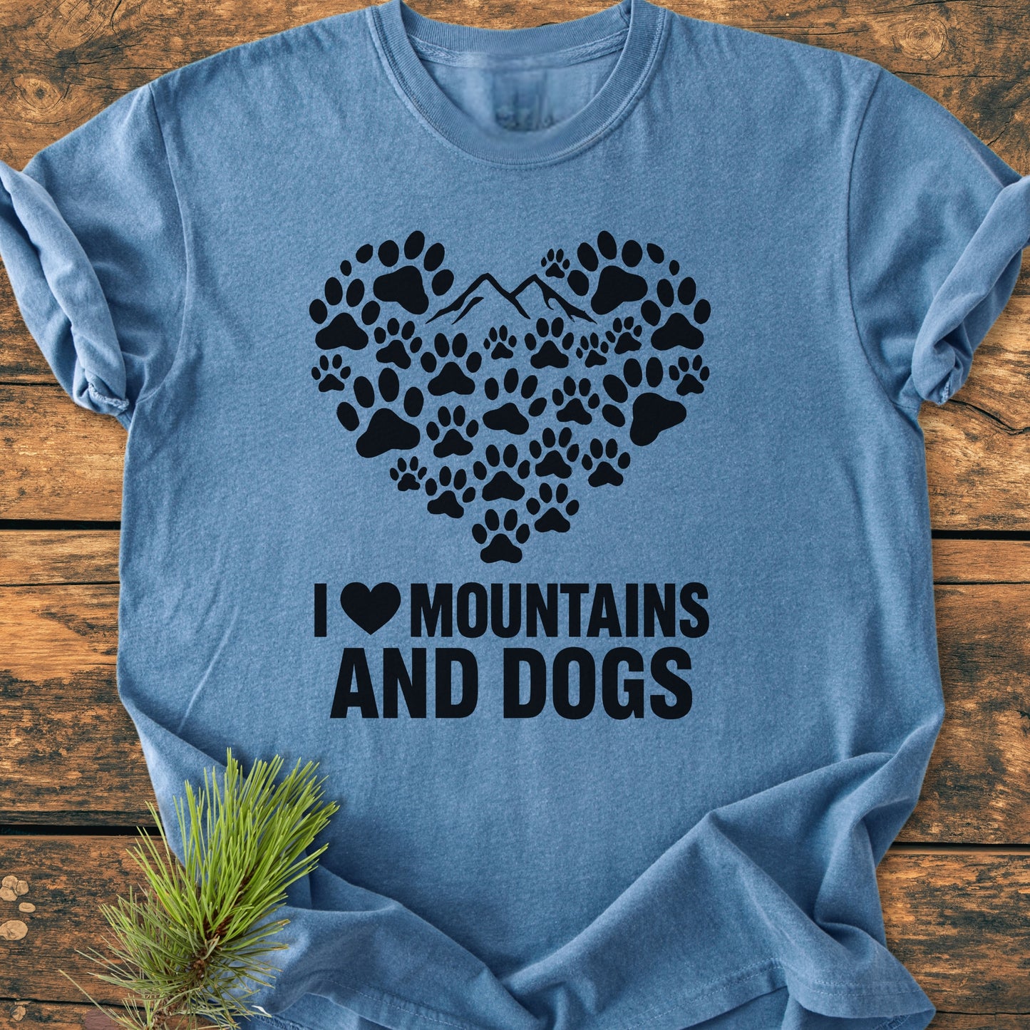 Paw Heart Dog Lover - Vintage Heavyweight Tee features a heart graphic of paw prints and mountains, with I ♥ MOUNTAINS AND DOGS text. Displayed flat with a pine sprig beside it.