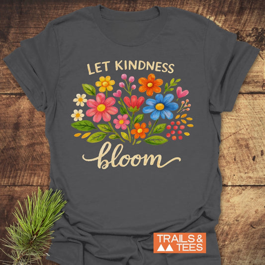 Let Kindness Bloom T-Shirt featuring a hand-painted flower bouquet and script text, laid on wood. Includes Trails & Tees logo. Made from soft cotton, perfect for outdoor adventures.