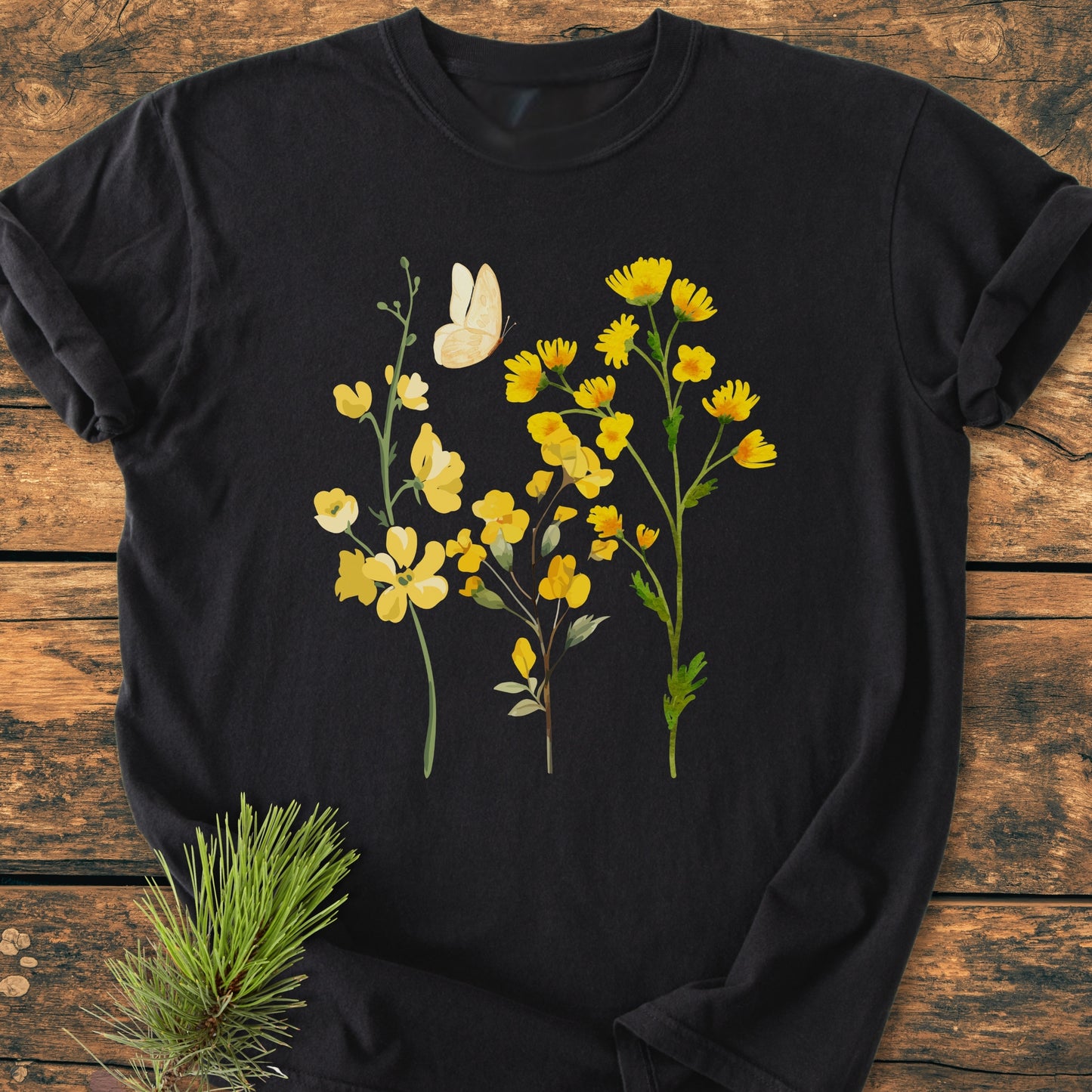 Yellow Boho Flowers - Vintage Heavyweight Tee features black, short-sleeve tee with yellow wildflowers and a cream butterfly graphic, displayed on a wooden surface, highlighting its relaxed fit and soft cotton fabric.
