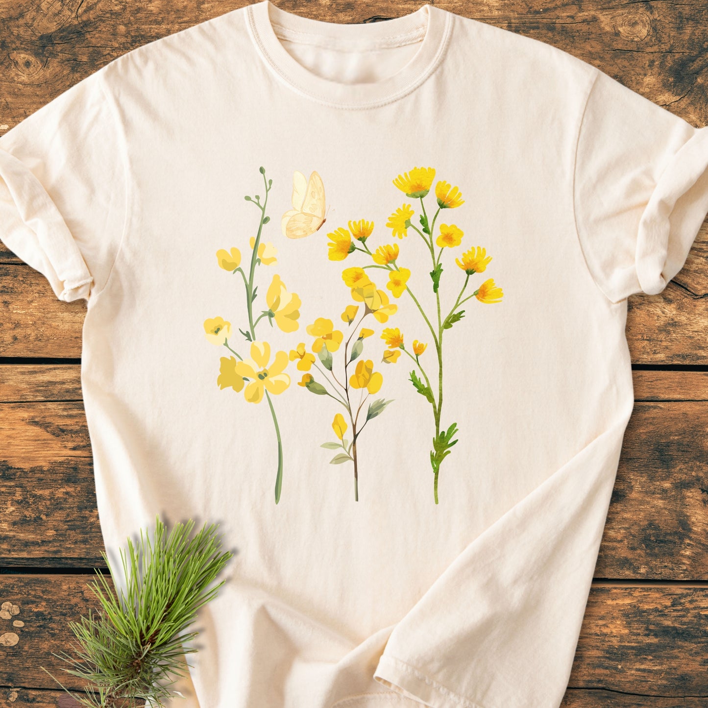 Yellow Boho Flowers - Vintage Heavyweight Tee: Cream T-shirt with three yellow wildflower stems and a butterfly design, laid on rustic wood. Includes a pine sprig accent. Made of soft, garment-dyed cotton.