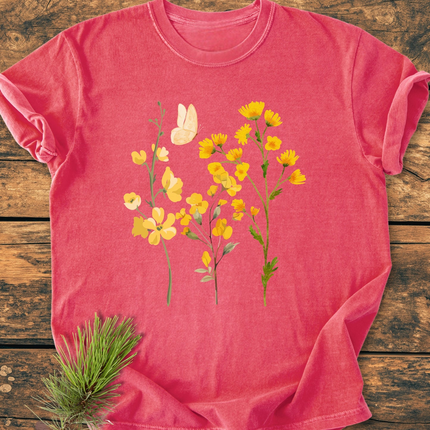 Yellow Boho Flowers - Vintage Heavyweight Tee featuring a graphic of yellow wildflowers and a butterfly, laid flat on a wooden surface, highlighting its soft-washed texture and relaxed fit.