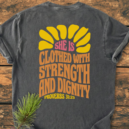 Strength And Dignity BACK PRINT - Vintage Wash Tee displayed on wood, featuring a retro half-sun graphic with empowering text and Proverbs 31:25. Made from soft, garment-dyed 100% ring-spun cotton.