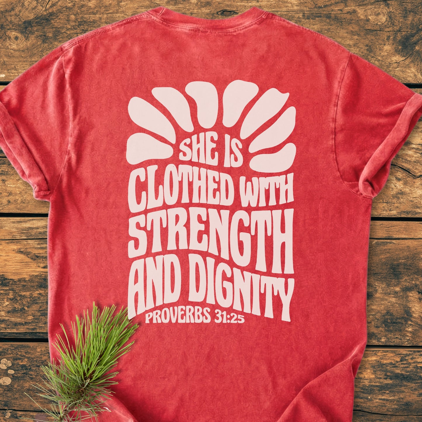 Strength And Dignity BACK PRINT - Vintage Wash Tee, featuring bold white lettering and a sunburst graphic, laid flat on wood. A red, stone-washed design emphasizes comfort and durability with its relaxed fit.