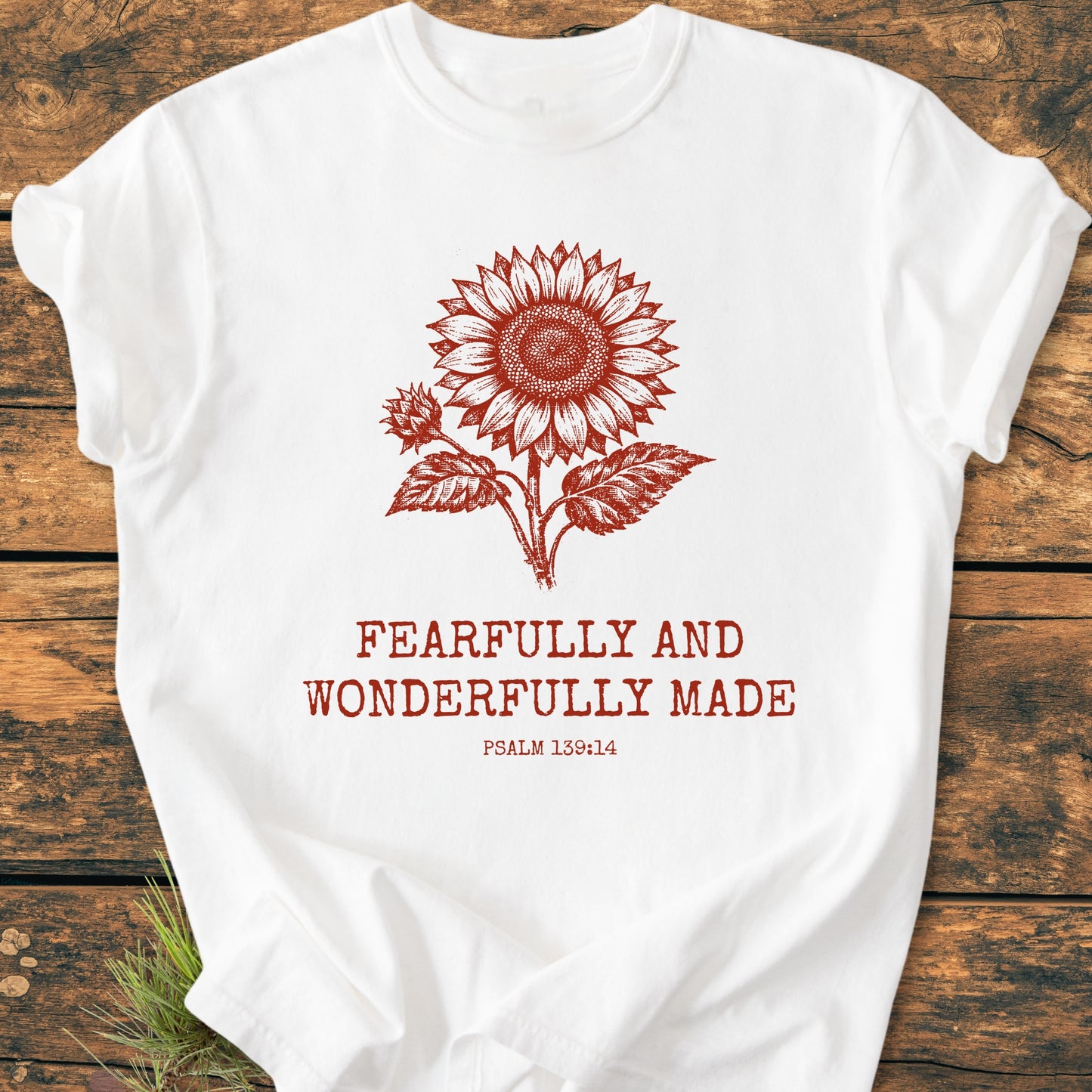 Fearfully And Wonderfully Made, Psalm 139:14 - Vintage Wash Tee features a red-tone sunflower illustration and scripture on a white Comfort Colors 1717 T-shirt, laid on a wooden surface.