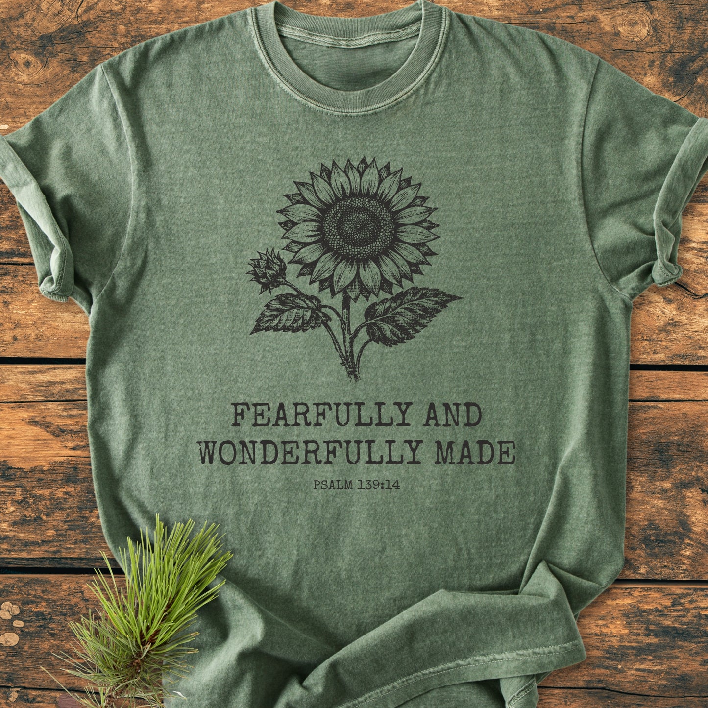 Heathered green Fearfully And Wonderfully Made, Psalm 139:14 - Vintage Wash Tee, featuring a black sunflower line-drawing, laid on rustic wood with pine sprig, highlighting comfort and durability.