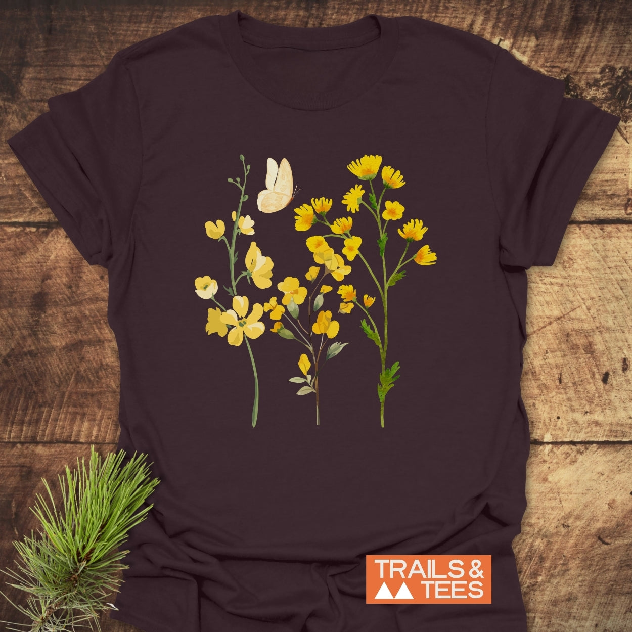 Yellow Boho Flowers T-Shirt on rustic wood, featuring three yellow wildflower stems and a butterfly graphic, with TRAILS & TEES logo. Soft, lightweight, and perfect for outdoor adventures.