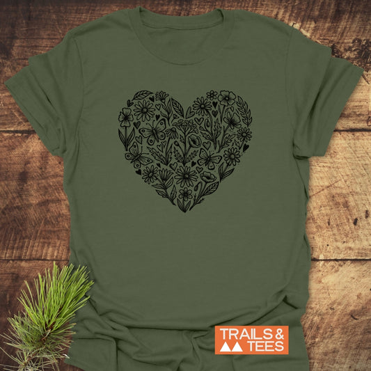 Wildflower Heart Butterfly Soul Softstyle T-Shirt features a large heart with hand-drawn wildflowers, leaves, hearts, and butterflies. Displayed flat on wood, it includes the TRAILS & TEES logo.