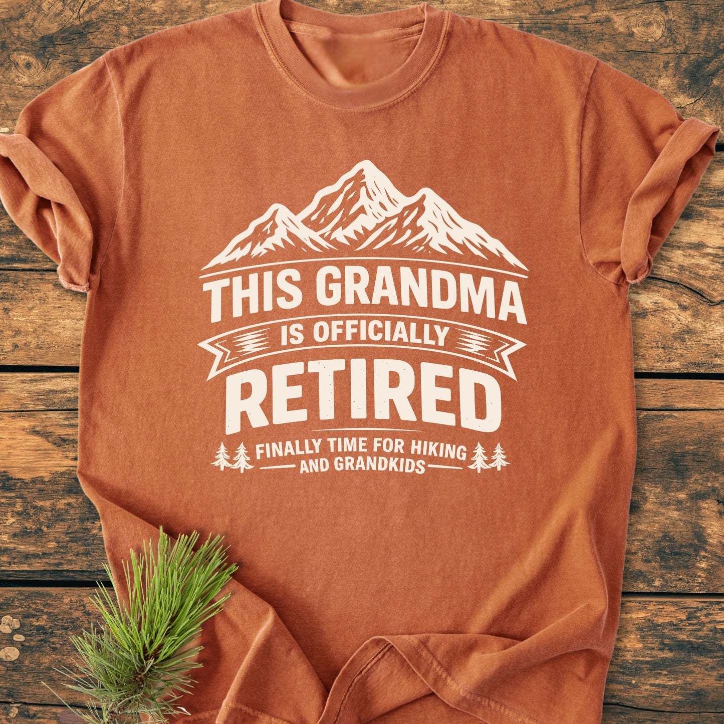 This Grandma is Officially Retired - Vintage Wash Tee features a stylized mountain design and text, laid on wood with a pine sprig; a soft, relaxed fit, 100% cotton garment.