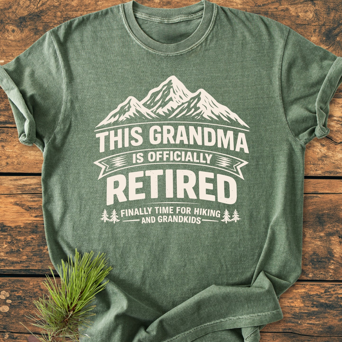 Heather-green This Grandma is Officially Retired - Vintage Wash Tee with mountain graphic and text, laid flat on wood. Features soft, garment-dyed fabric and relaxed fit, perfect for leisure activities.