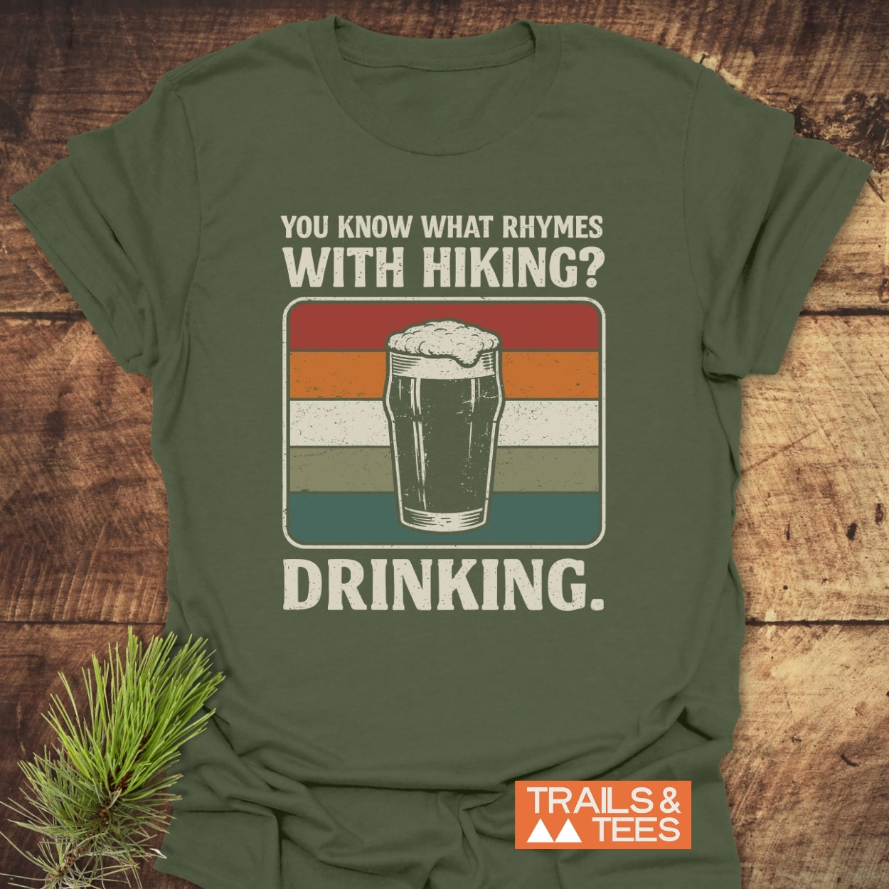 What Rhymes With Hiking? Softstyle T-Shirt: Forest-green tee with retro pint glass graphic, humorous hiking and drinking text, and Trails & Tees logo, perfect for outdoor and casual wear.