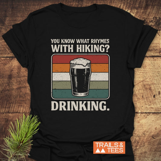 What Rhymes With Hiking? Softstyle T-Shirt features a retro striped graphic with a pint glass and humorous slogan, perfect for hikers who enjoy post-adventure drinks.