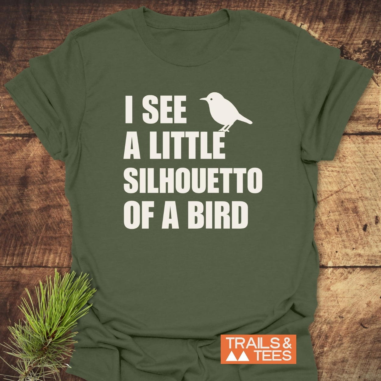 Silhouetto Of A Bird Funny Softstyle T-Shirt displayed on wood, featuring a white bird silhouette design and text. Includes Trails & Tees logo; made from soft, lightweight, ring-spun cotton for everyday comfort.