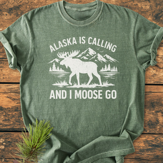 Alaska Is Calling - Vintage Wash Tee: Green T-shirt with a white wilderness scene and playful text. Soft, relaxed fit, perfect for everyday wear, capturing a vintage aesthetic.