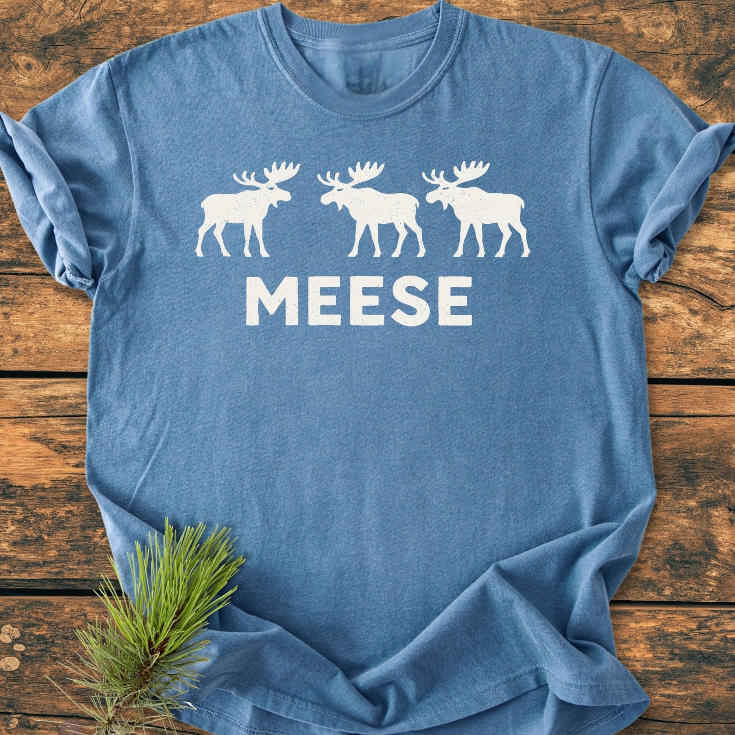 Heather-blue T-shirt showing three white moose silhouettes and MEESE text; embodies outdoor humor and vintage style, perfect for moose enthusiasts.