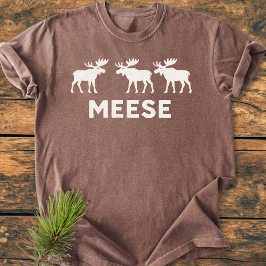 Meese - Vintage Wash Tee featuring three moose silhouettes and MEESE text in white, laid on wood with a pine sprig, embodies rustic outdoor humor in a relaxed, soft-washed fit.