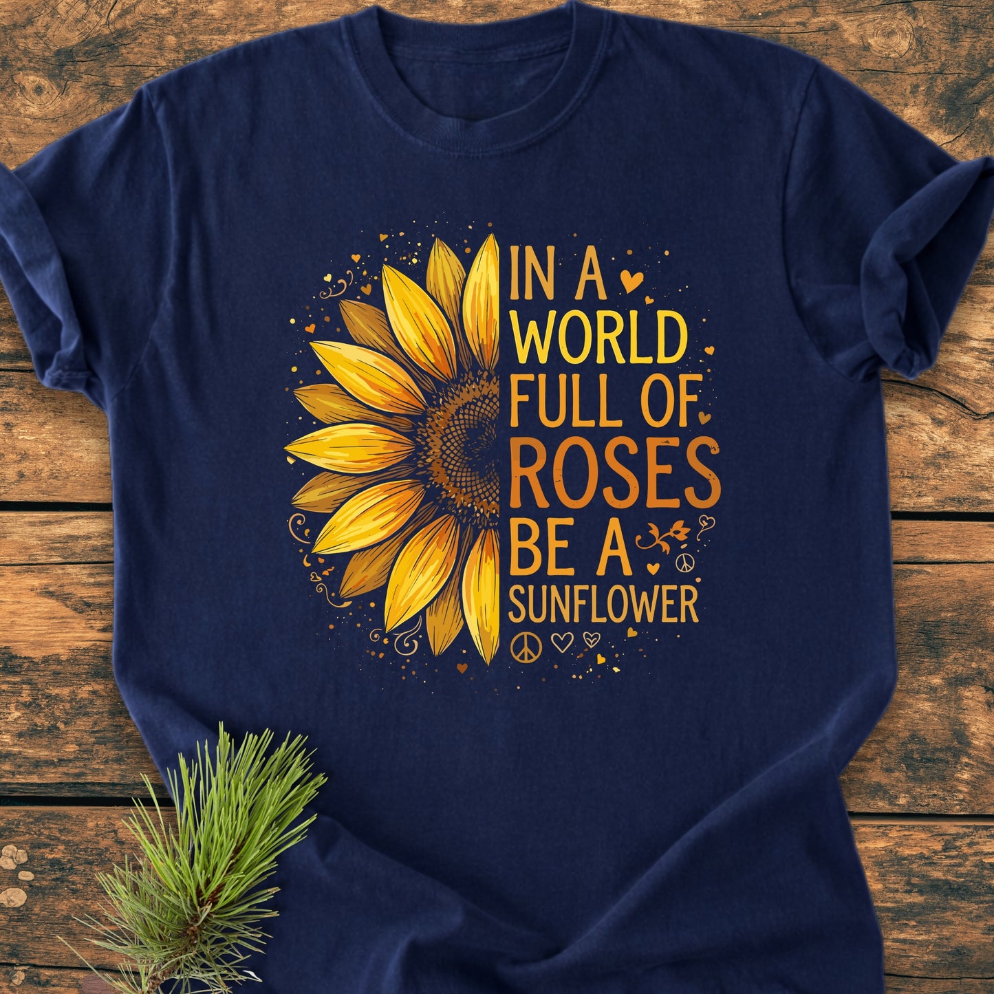 Navy-blue Be A Sunflower - Vintage Wash Tee with a bright half-sunflower graphic and uplifting slogan, laid on wood with pine sprig. Ideal for nature enthusiasts and individuality supporters.