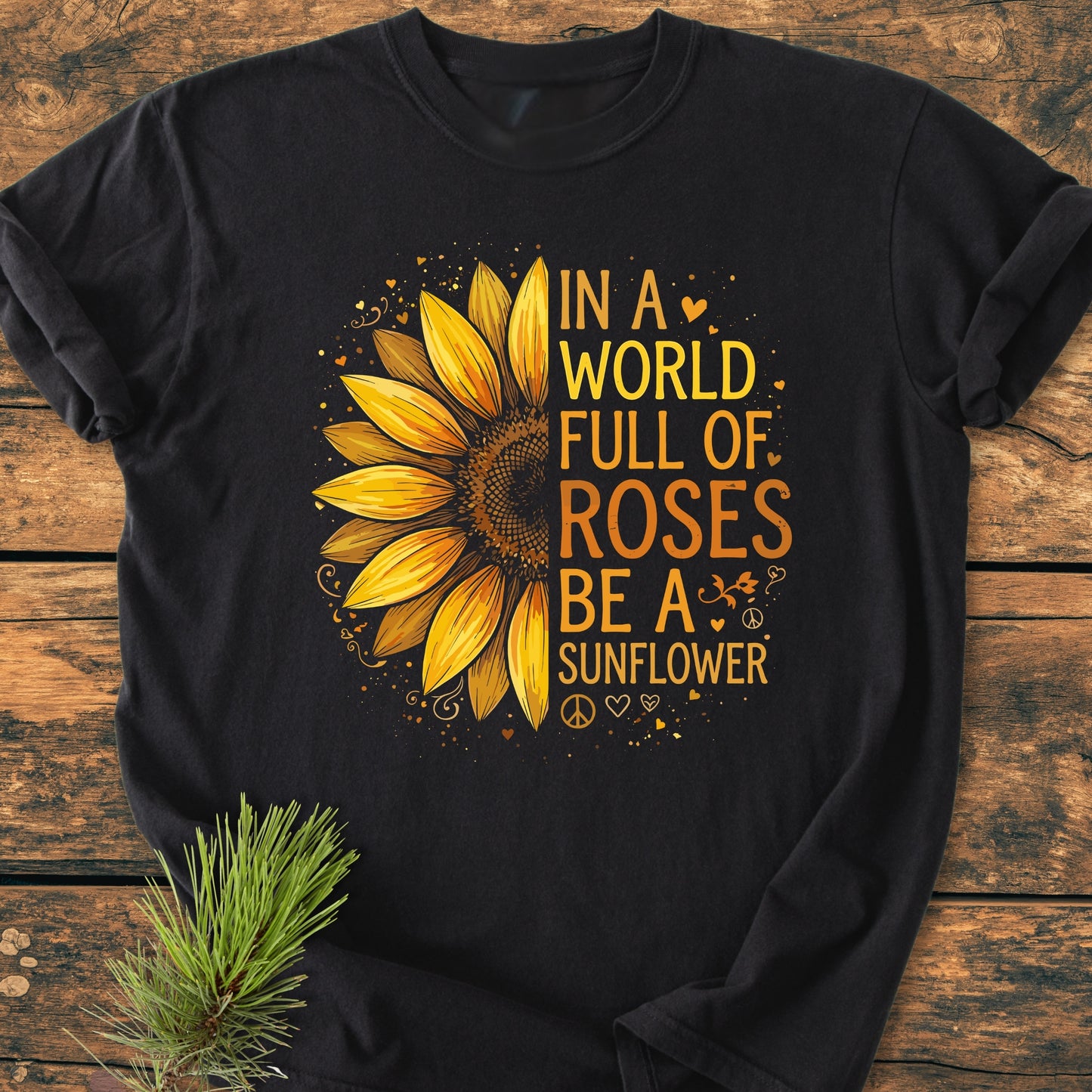 Be A Sunflower - Vintage Wash Tee featuring a large half-sunflower graphic with an inspiring phrase, surrounded by hearts and peace signs, displayed on a rustic wooden surface with a pine sprig.