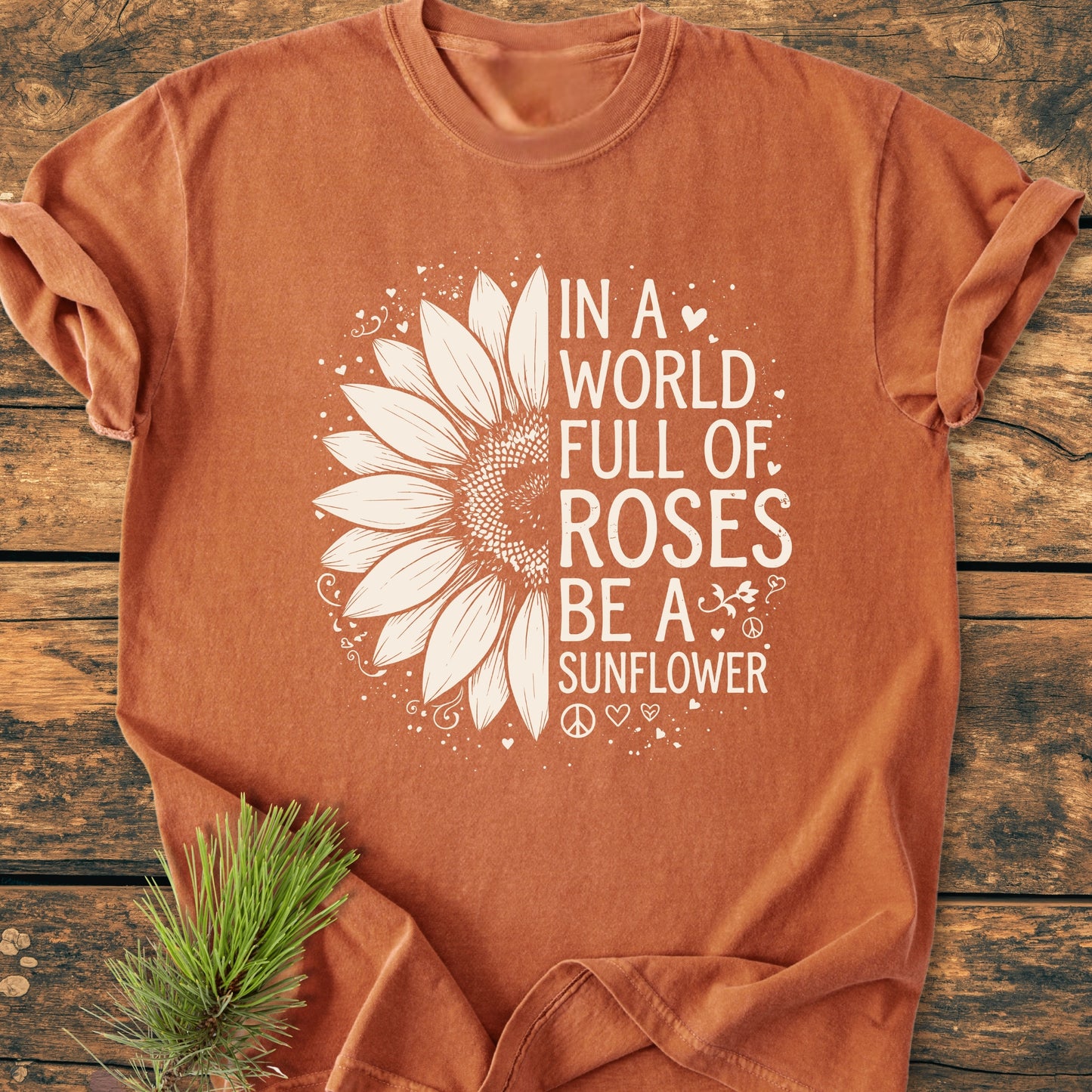 Be A Sunflower - Vintage Wash Tee: Rust-orange T-shirt with white sunflower graphic and motivational text, laid on wood, styled with pine needles, embodying a nature-inspired, relaxed unisex fit.