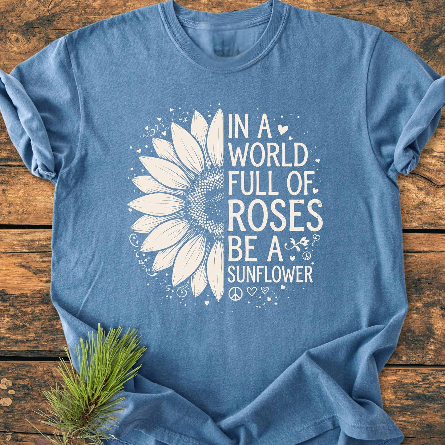 Be A Sunflower - Vintage Wash Tee featuring a half sunflower and positive message, laid flat with a spruce branch accent. Perfect for nature lovers seeking individuality and comfort.