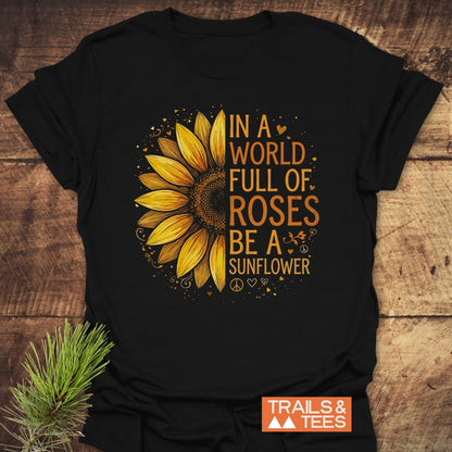 The Be A Sunflower Softstyle T-Shirt features a sunflower graphic with the slogan In a world full of roses be a sunflower, surrounded by decorative elements, on a black tee.