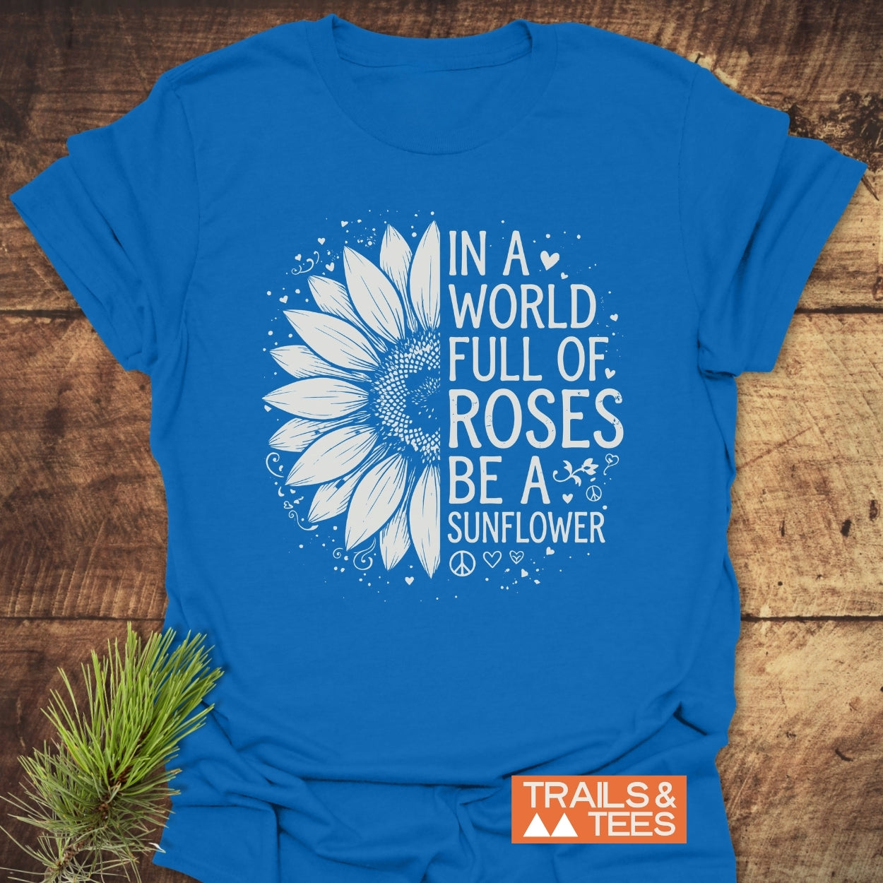 Be A Sunflower Softstyle T-Shirt features a white half-sunflower graphic with hearts and swirls on a royal-blue tee, alongside the phrase promoting individuality and positivity.