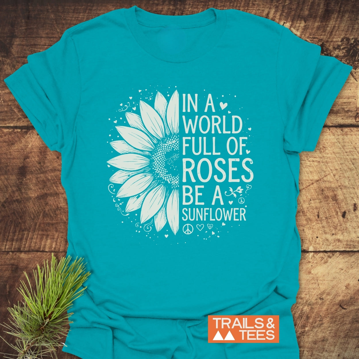 Be A Sunflower Softstyle T-Shirt features a sunflower design and uplifting phrase, ideal for nature lovers. Enhanced with doodles, it lays flat beside pine sprigs, showcasing its vibrant print and soft texture.
