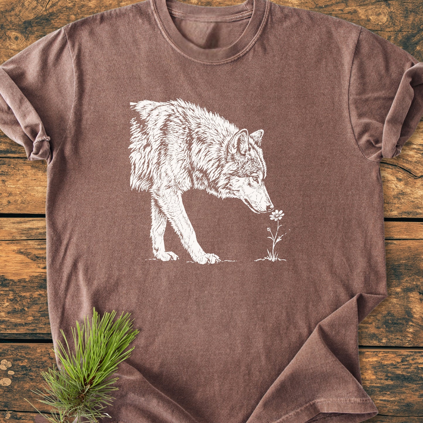 Stop And Smell The Flowers - Vintage Wash Tee featuring a wolf sniffing a flower, displayed on a wooden surface with pine needles, embodies a gentle nature aesthetic and relaxed outdoor vibe.