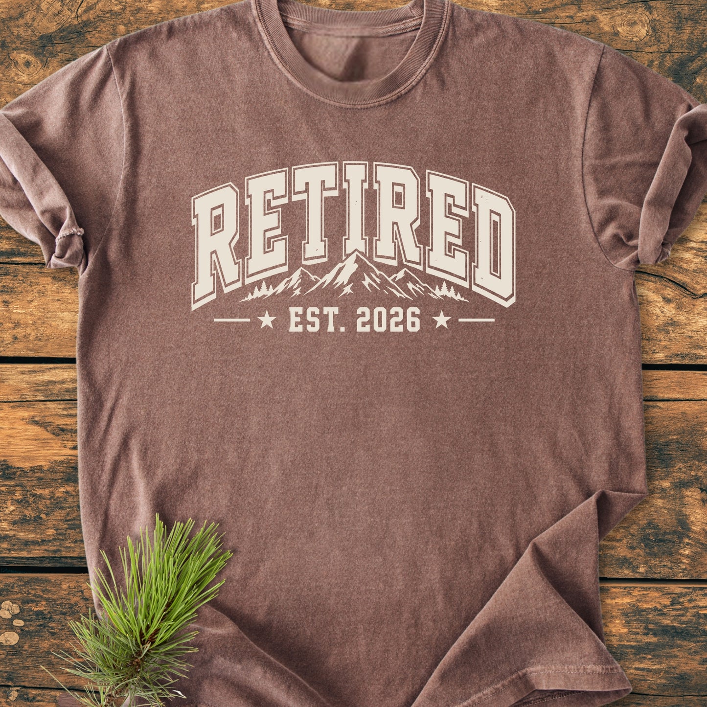 Retired 2026 - Vintage Wash Tee with collegiate print, mountain and tree line-drawing, on rustic wood. Pine bough accent. Perfect for retirees and mountain lovers embracing outdoor adventures.