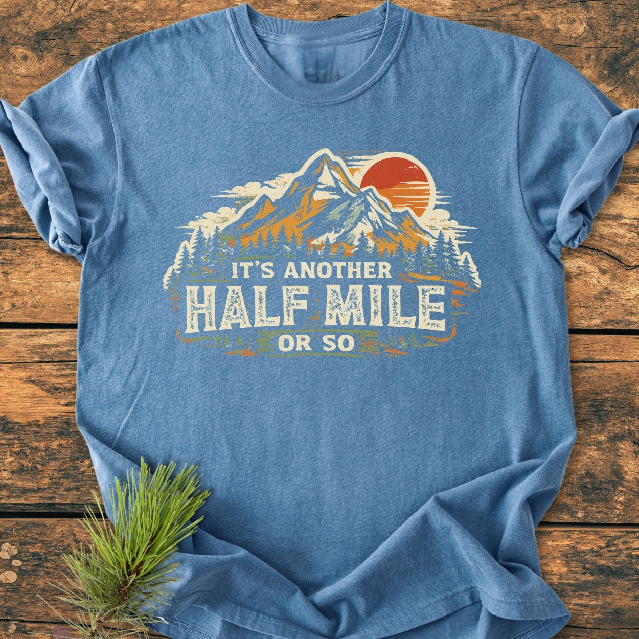 Another Half Mile Or So - Vintage Wash Tee featuring a mountain sunset graphic and pine trees, laid flat. Soft, relaxed fit, perfect for hiking enthusiasts. Suitable for everyday wear, built for durability.