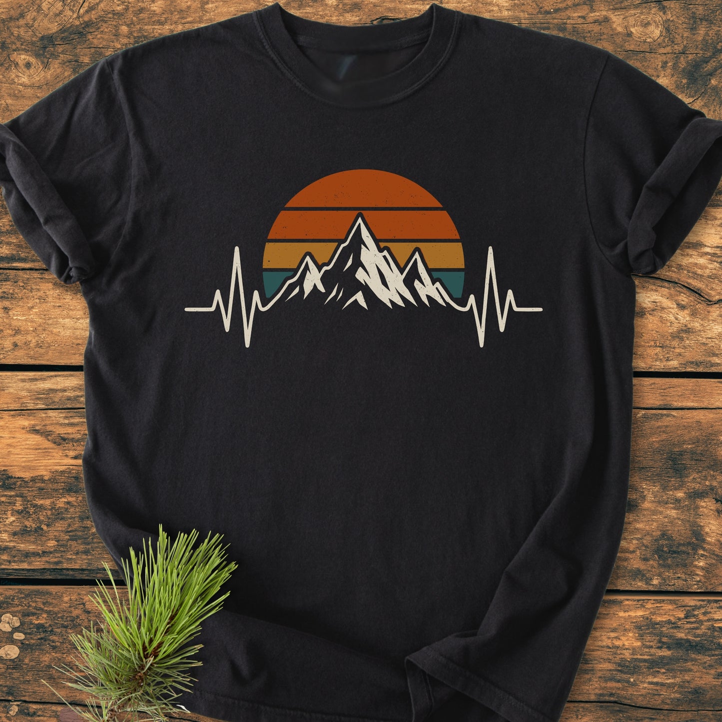 Mountain Heartbeat - Vintage Wash Tee: Black long-sleeve T-shirt with mountain-peak and EKG-line print, laid on wooden surface, accented by a pine sprig; embodies a hiker's passion and relaxed fit.