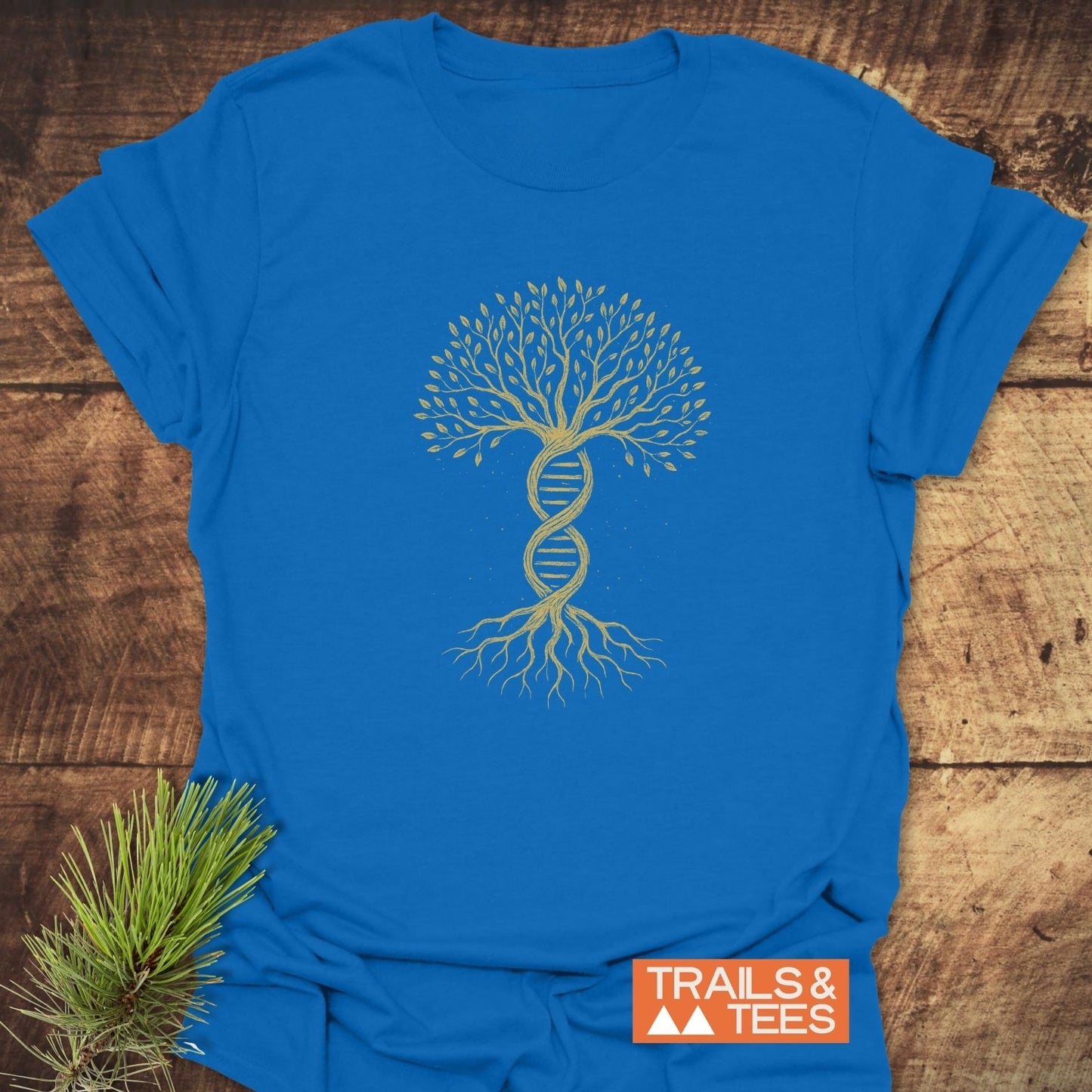Tree Of Life T-Shirt featuring a DNA double-helix tree graphic, laid flat beside a pine sprig, perfect for nature lovers, made from soft, lightweight ring-spun cotton by Trails & Tees.