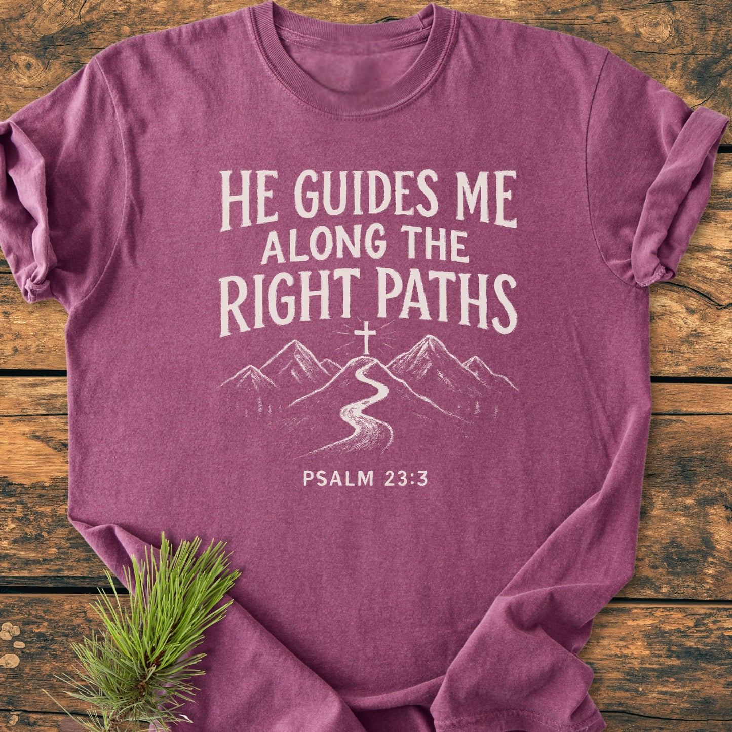 He Guides Me - Vintage Wash Tee: Heathered purple T-shirt featuring a white mountain path design with “He guides me along the right paths” and “Psalm 23:3” on a rustic wood backdrop with pine sprig.
