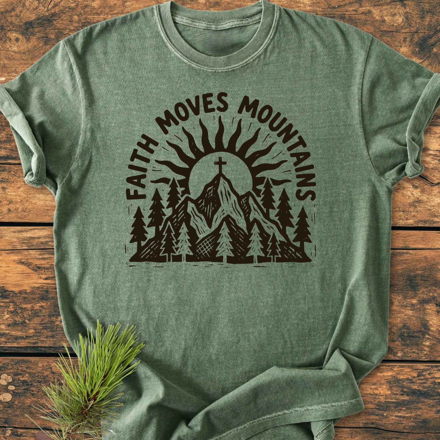 The 1409 Faith Moves Mountains T-shirt features a mountain design with pine trees and a cross, set against a wooden backdrop, highlighting Comfort Colors' soft-washed, relaxed fit tee.