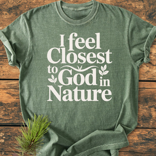 Olive-green 1427 Closest To God - Vintage Wash Tee features white lettering and leaf motifs, laid on wood with a pine sprig. Relaxed fit, garment-dyed for a vintage feel.
