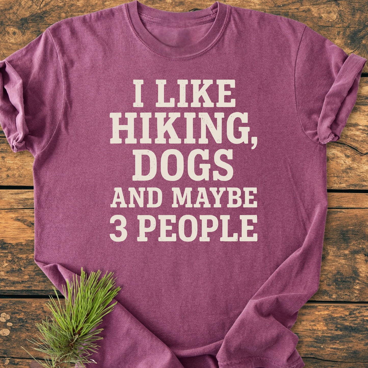 Purple T-shirt with I LIKE HIKING, DOGS AND MAYBE 3 PEOPLE in white letters, showcasing Trails & Tees' relaxed fit, vintage wash style, on a wooden surface with a pine sprig.