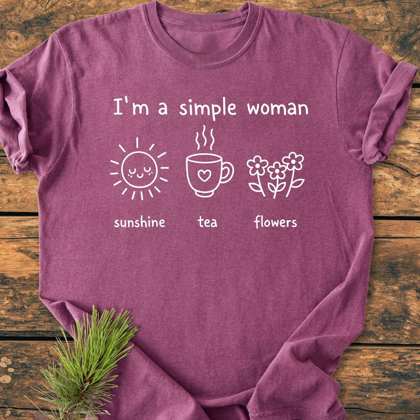 Heathered plum-colored 1408 I'm A Simple Woman T-shirt features white text with icons: sun, tea, flowers. Laid flat on wood with a pine sprig. Comfortable, relaxed fit, 100% ring-spun cotton.