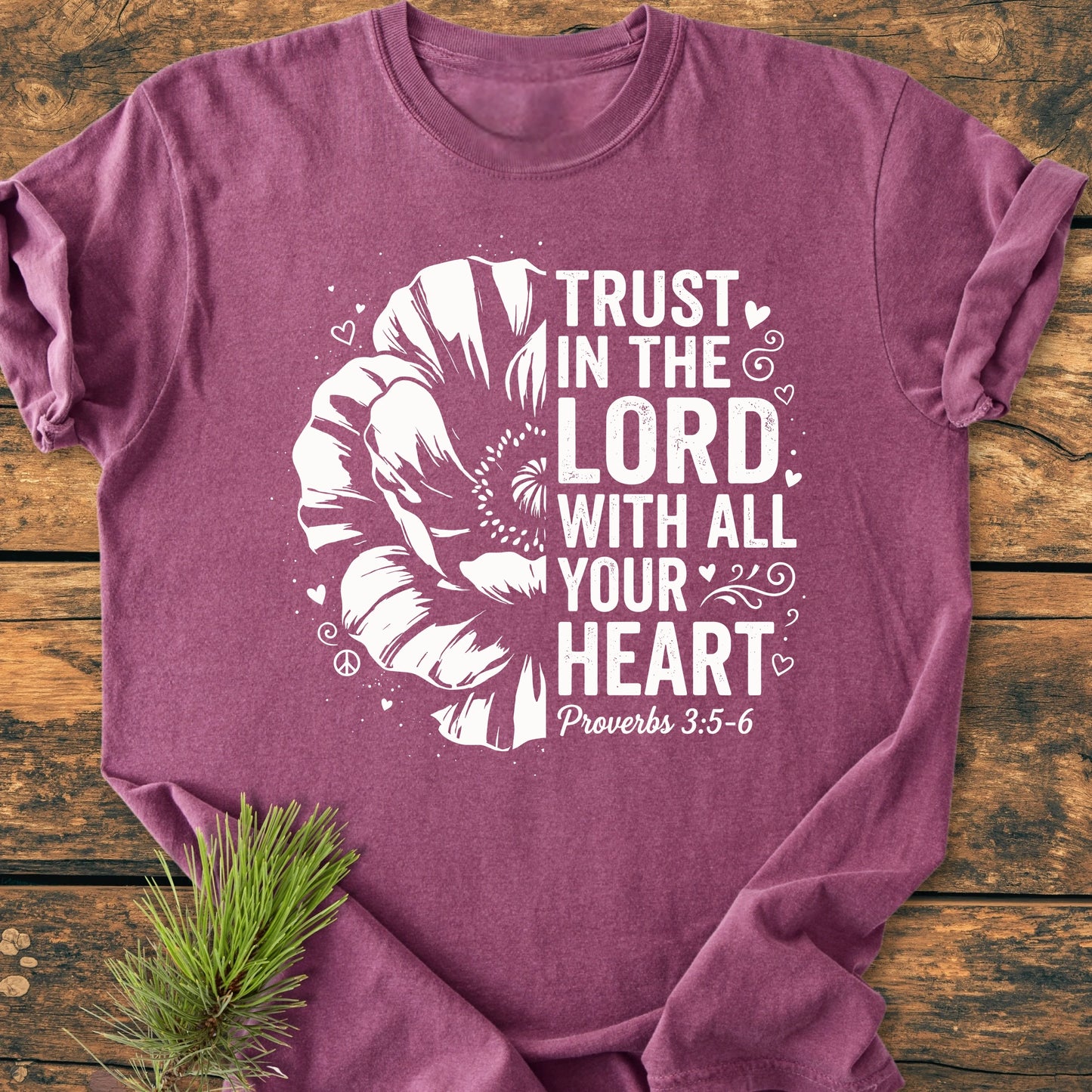 Heathered purple Trust In The Lord - Vintage Wash Tee with a white stylized flower and scripture text, laid on rustic wood with a pine sprig.