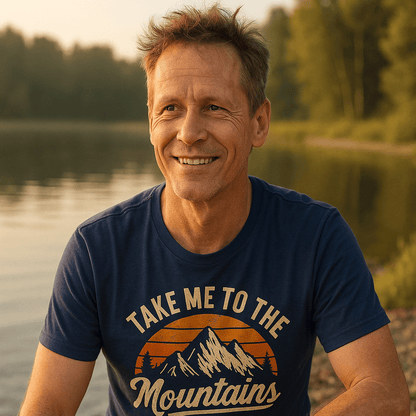 Middle-aged man outdoors wearing Take Me To The Mountains T-shirt, featuring a sunset and mountain design. Ideal for adventures with its soft, lightweight cotton.