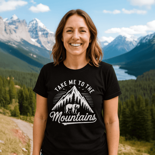 Woman on mountain trail wearing Take Me To The Mountains T-shirt with mountain graphic, designed for comfort and adventure.