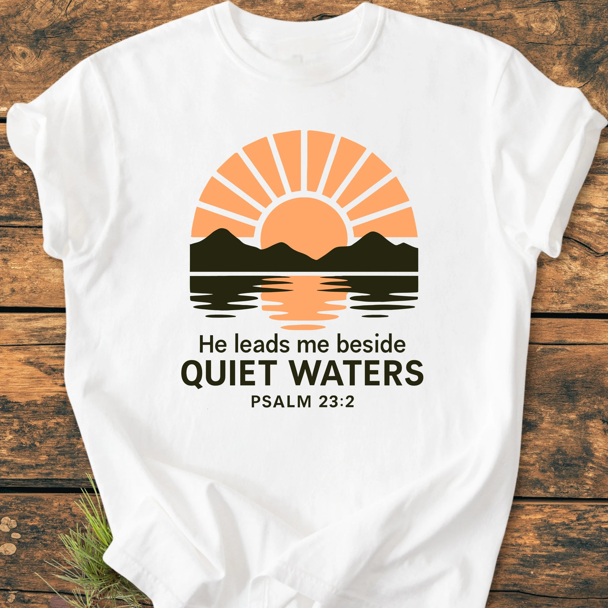 White T-shirt featuring 1424 He Leads Me with a sunrise graphic over mountains, Psalm 23:2 text. Laid flat, showcasing relaxed fit and vintage wash texture for everyday wear.