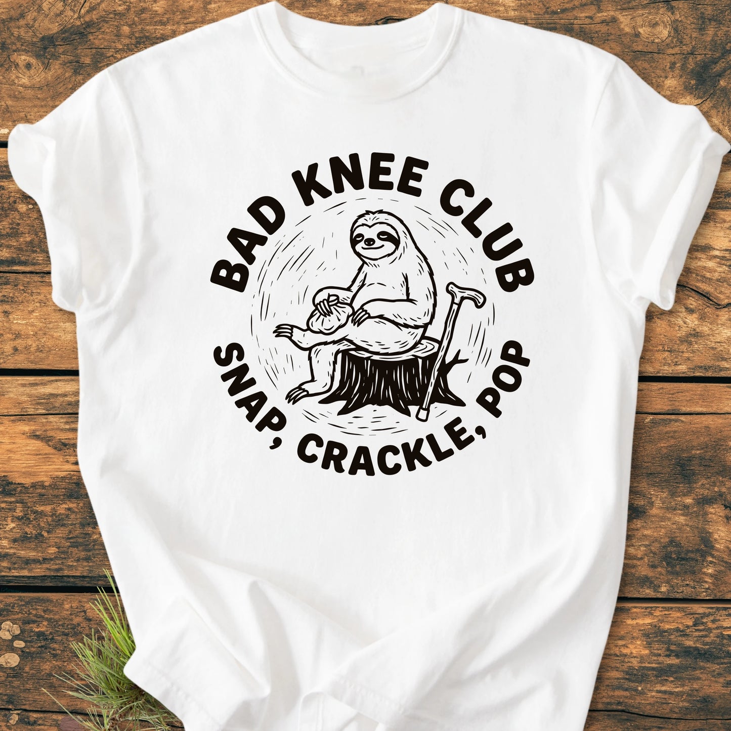 White T-shirt featuring a cartoon sloth on a stump with BAD KNEE CLUB text, capturing a playful vibe. Designed for comfort with vintage wash and durable stitching, ideal for everyday wear.