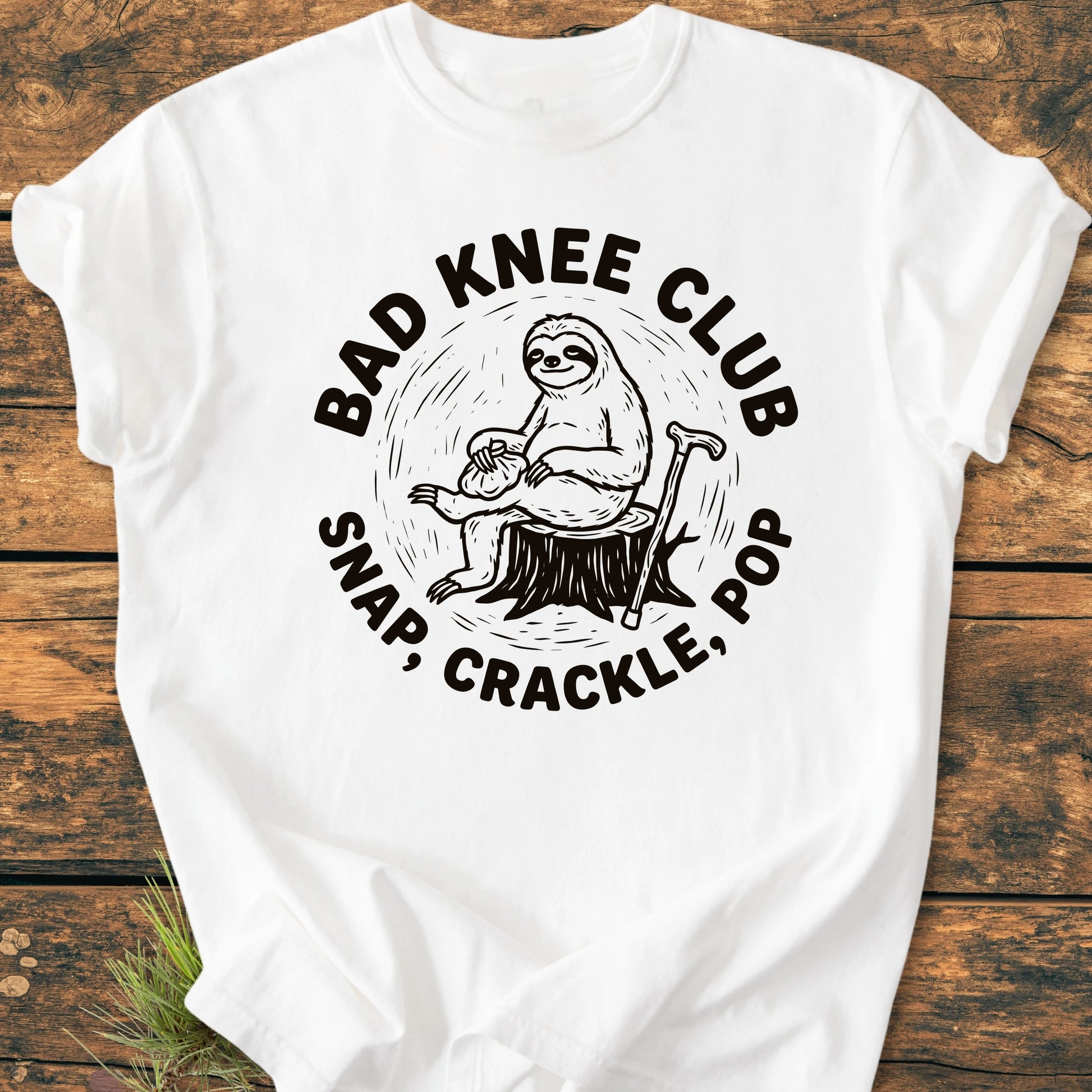 White T-shirt featuring a cartoon sloth on a stump with BAD KNEE CLUB text, capturing a playful vibe. Designed for comfort with vintage wash and durable stitching, ideal for everyday wear.