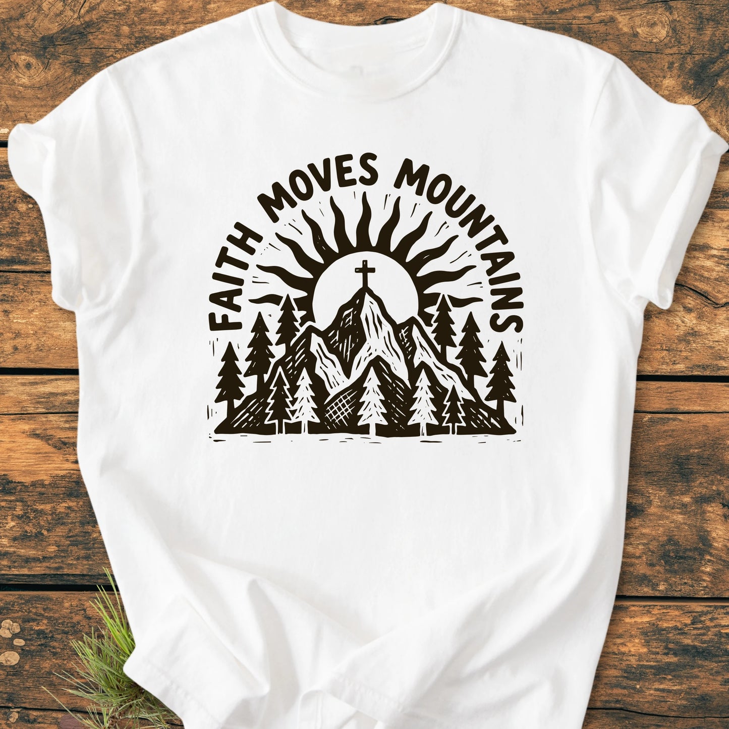 1409 Faith Moves Mountains T-shirt features a mountain scene with pine trees, a sun, and a cross on the summit, complemented by the slogan. Crafted from soft, durable, 100% ring-spun cotton.