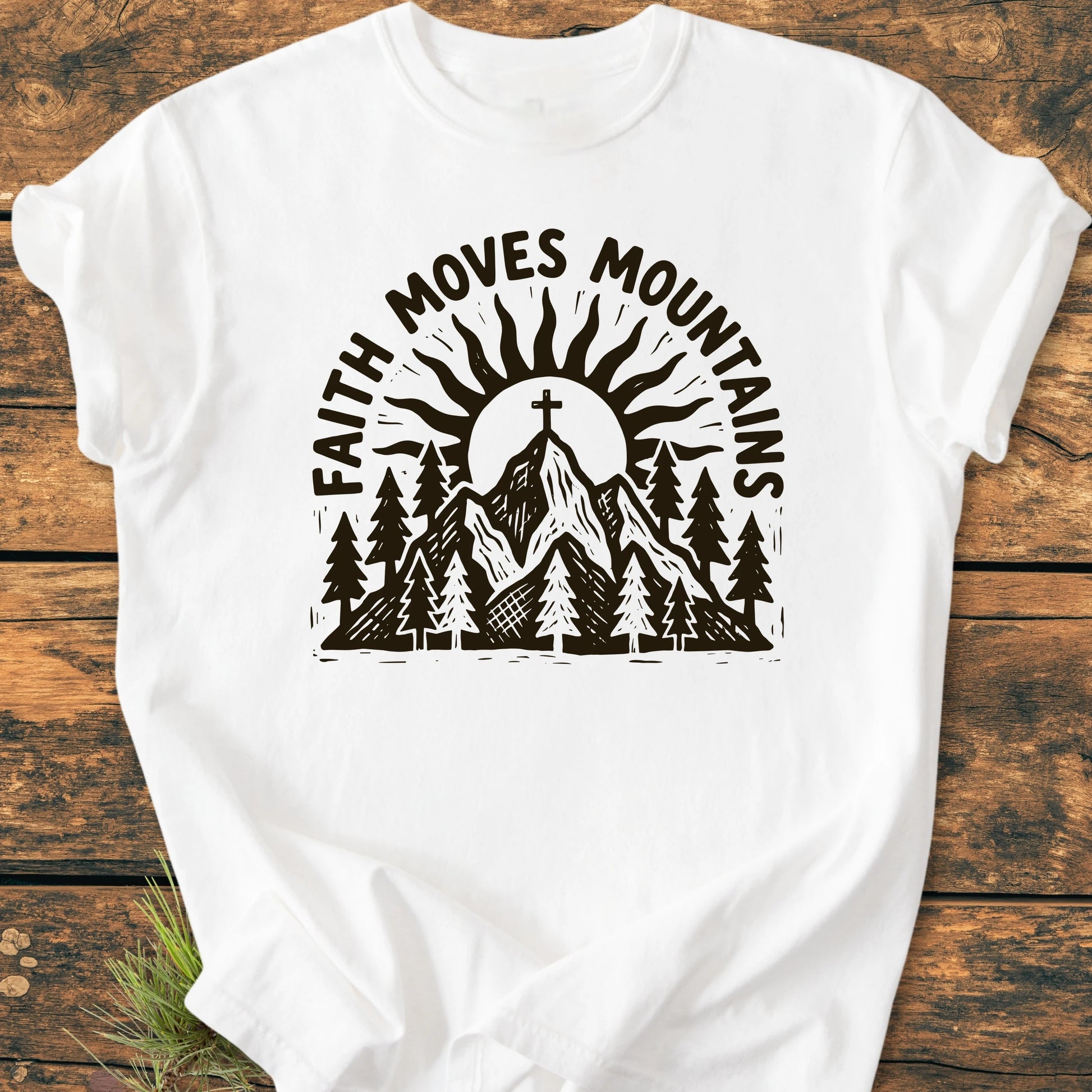 1409 Faith Moves Mountains T-shirt features a mountain scene with pine trees, a sun, and a cross on the summit, complemented by the slogan. Crafted from soft, durable, 100% ring-spun cotton.