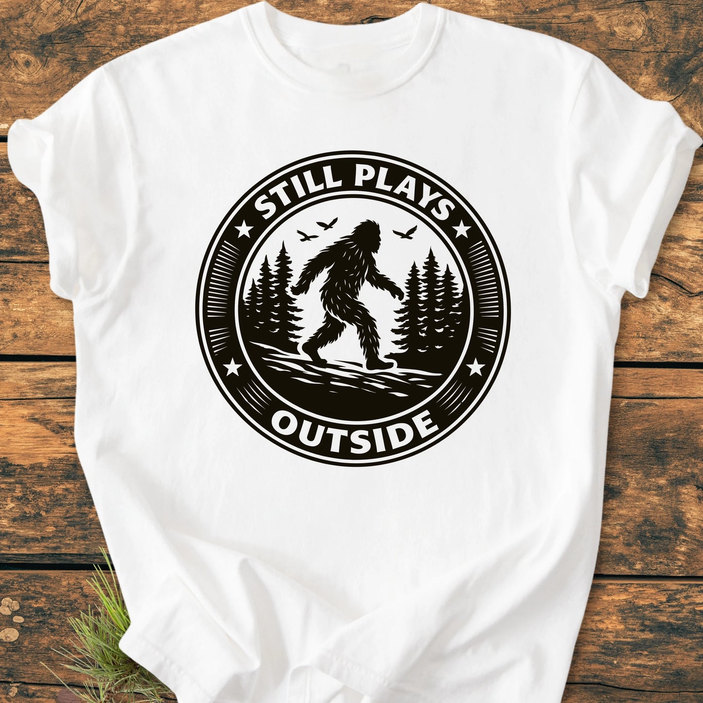 1430 Still Plays Outside Bigfoot T-shirt featuring a Sasquatch graphic amidst a pine forest. Relaxed unisex fit, vintage wash, soft garment-dyed cotton, ideal for outdoor enthusiasts seeking comfort and style.
